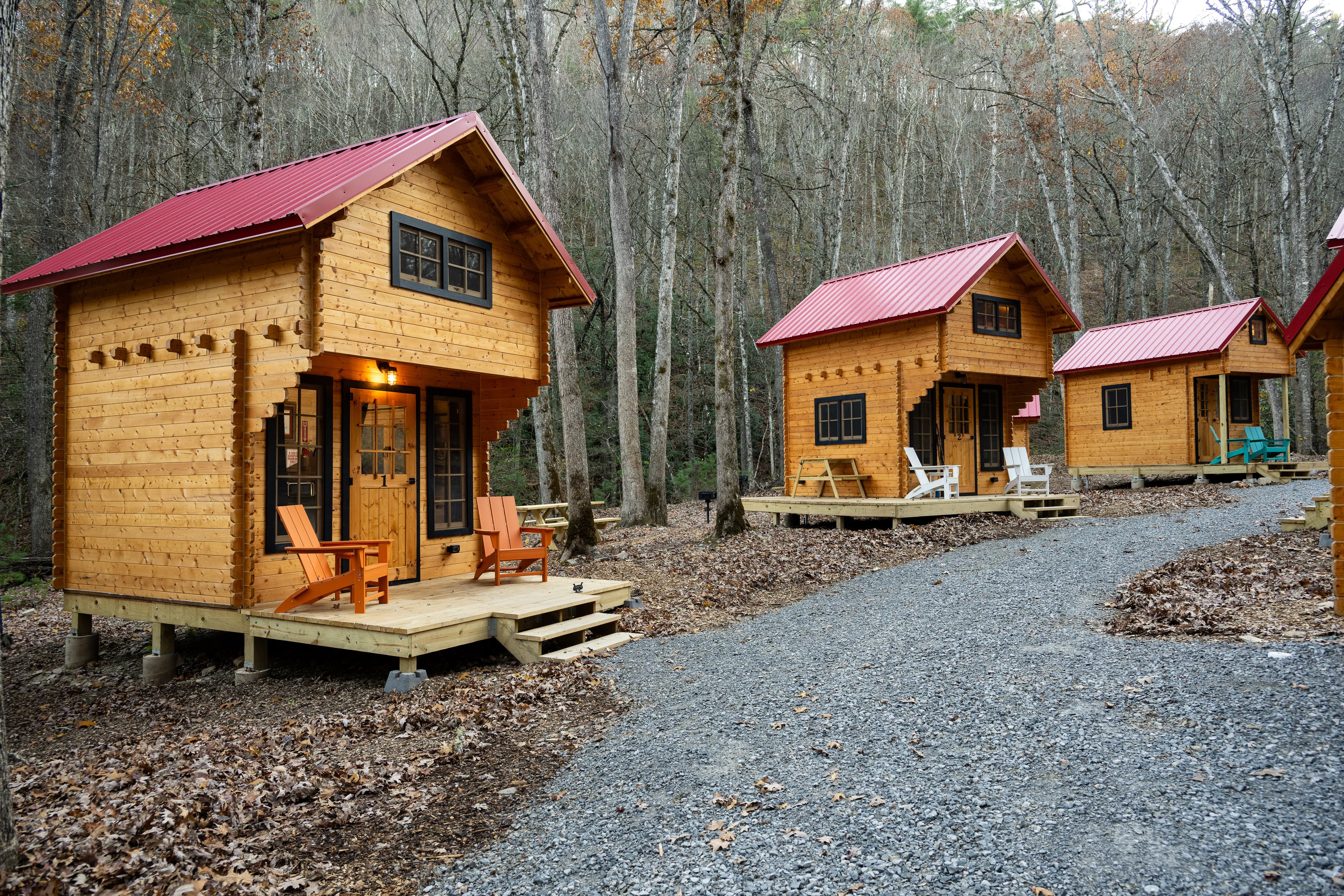 Three wooden cabins with red roofs on a gravel pathway surrounded by trees.