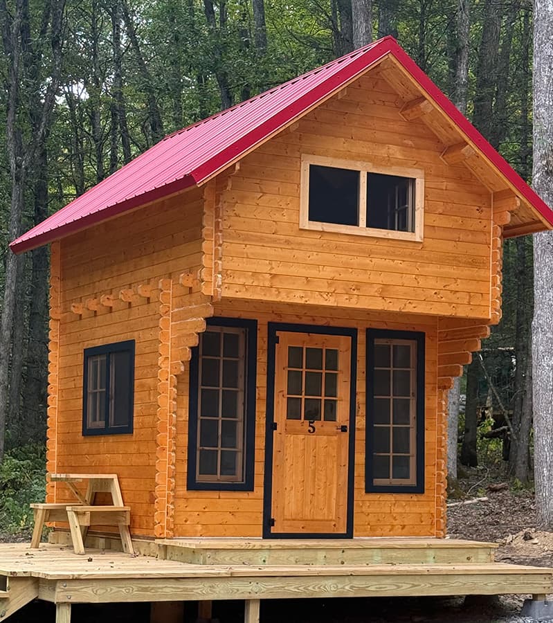 A small wooden cabin with a red roof surrounded by trees.