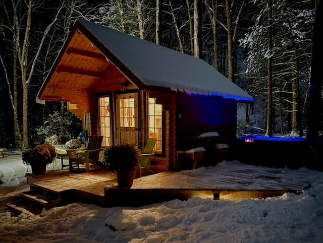 Cozy wooden cabin illuminated at night, surrounded by snow-covered trees.