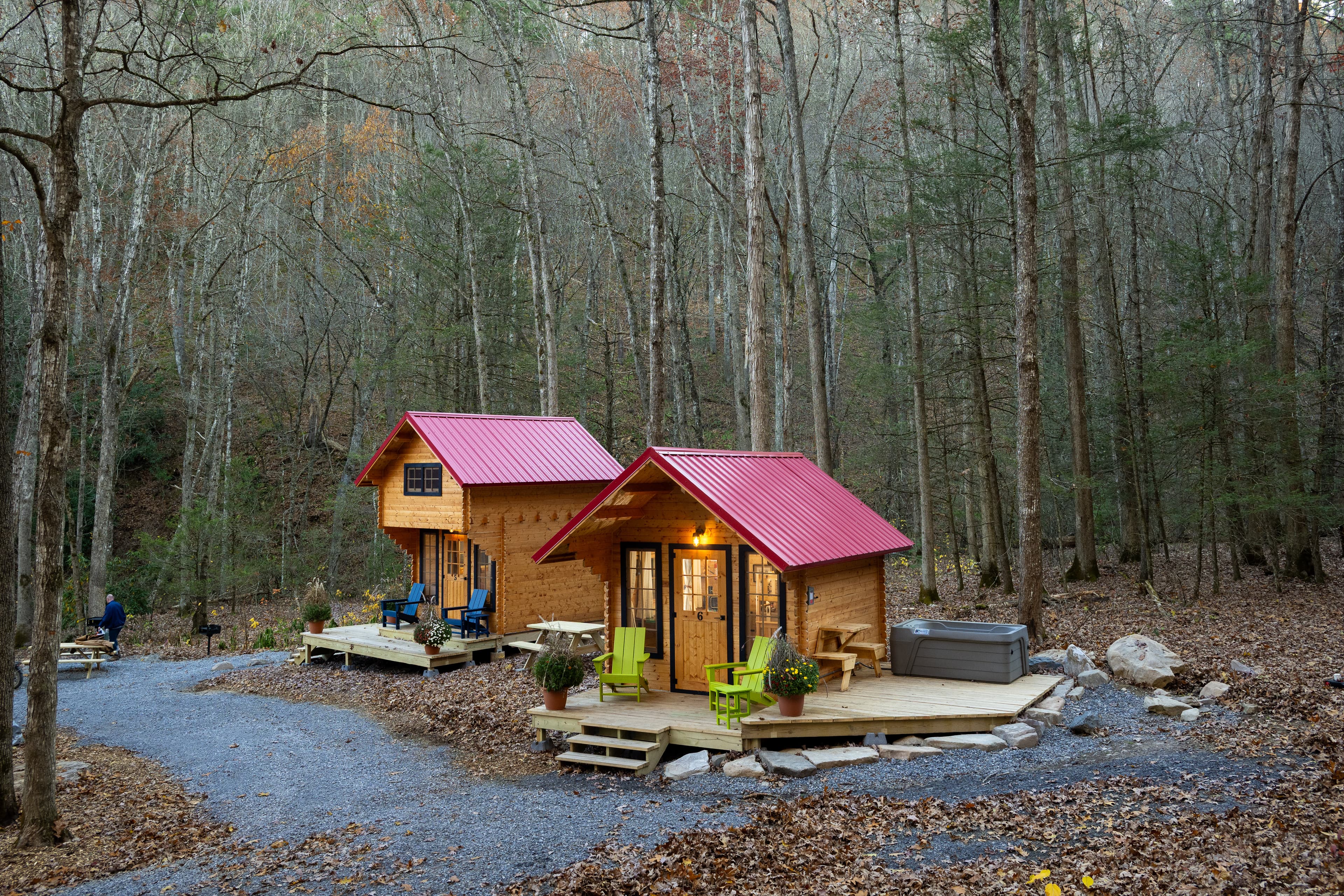 Two cozy cabins with red metal roofs nestled in a wooded area, surrounded by gravel pathways and autumn foliage.